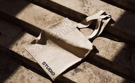 Canvas tote bag carrying the Studio wordmark, on stone steps