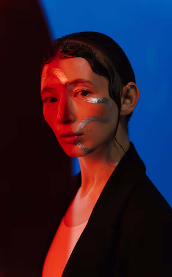 Studio portrait lit in red and blue, silver paint drawn across the face